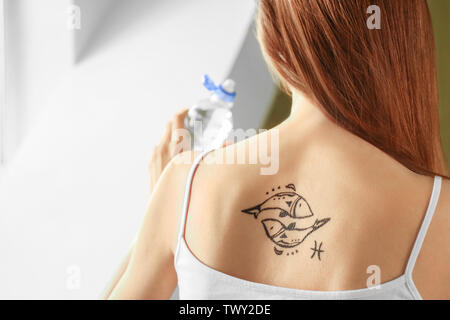 Donna con dipinto di pesci segno zodiacale sulla sua schiena in ambienti interni Foto Stock