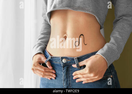 Donna con dipinto di LEO segno zodiacale sul suo ventre in ambienti interni Foto Stock