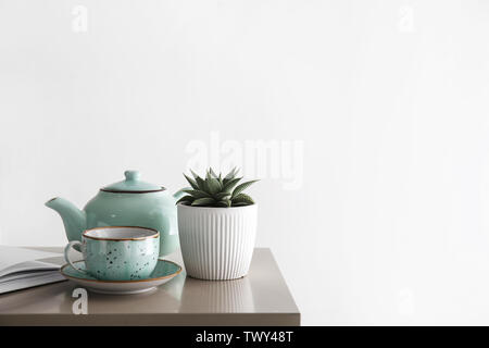 Succulenta in pentola con tazza e teiera sul tavolo in camera Foto Stock