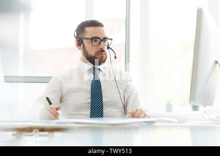 Grave concentrata barbuto tech support manager in camicia bianca e cravatta strippato seduti nella parte anteriore del computer e utente di consulenza su problemi sito web Foto Stock