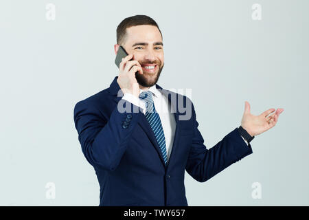 Fiducioso positivo maschi giovani manager in blu scuro tuta in piedi contro lo sfondo isolato e gesticolando mano durante la comunicazione sul telefono cellulare Foto Stock