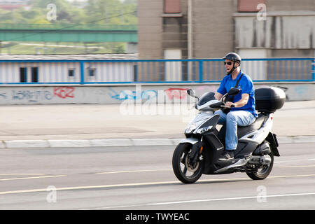 Belgrado, Serbia - Aprile 26, 2019: un uomo a cavallo di moto scooter oltre il ponte in città il traffico della strada Foto Stock