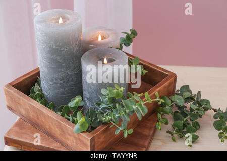 Scatola con candele accese e rami di eucalipto su tavola Foto Stock