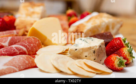 Fino vicino immagine di un piatto di antipasti con una miscela di carni fredde, fragole, crackers, formaggio e pane, con una profondità di campo ridotta Foto Stock