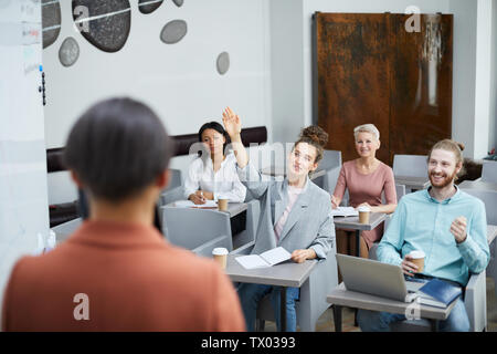 Ampio angolo ritratto contemporaneo di giovane donna alzando la mano in classe con gruppo di studenti godendo di una lezione, l'insegnante punto di vista Foto Stock