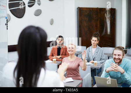 Ampio angolo ritratto di sorridere donna matura alzando la mano in classe con gruppo di studenti godendo di una lezione, insegnanti punto di vista Foto Stock