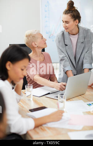 Ritratto di due imprenditrici contemporaneo utilizzando computer portatile mentre si discute dello sviluppo di un progetto in riunione Foto Stock