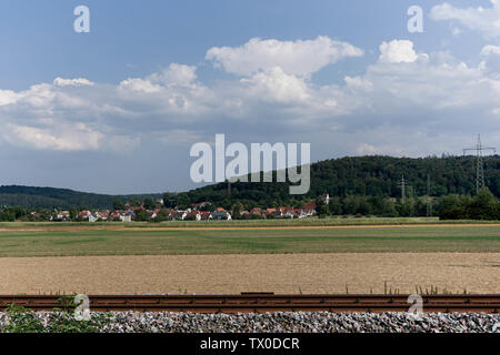 Ferrovia rustica, prato verde, piccola collina del villaggio e cielo blu nuvoloso. Paesaggio colorato vicino a Tubingen, Germania Foto Stock