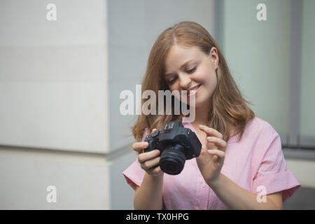 Ritratto di giovane donna caucasica photgrapher tenendo una fotocamera digitale, sorridente Foto Stock