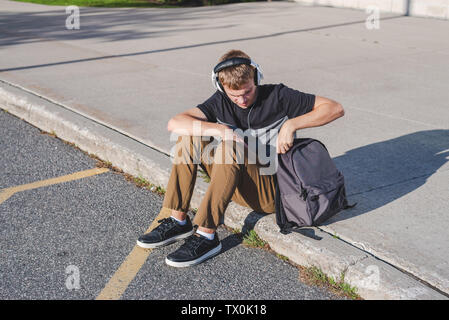 Felice ragazzo seduto per terra con il suo zaino mentre si ascolta la musica. Foto Stock