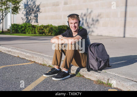 Felice ragazzo seduto per terra con il suo zaino mentre si ascolta la musica. Foto Stock