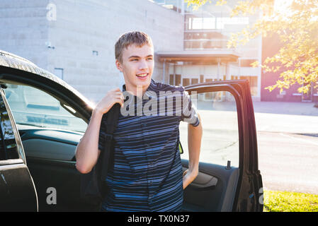 Felice adolescente di uscire la sua auto e la messa sul suo zaino come egli arriva a scuola la mattina. Foto Stock