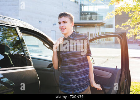 Felice adolescente di uscire la sua auto e la messa sul suo zaino come egli arriva a scuola la mattina. Foto Stock