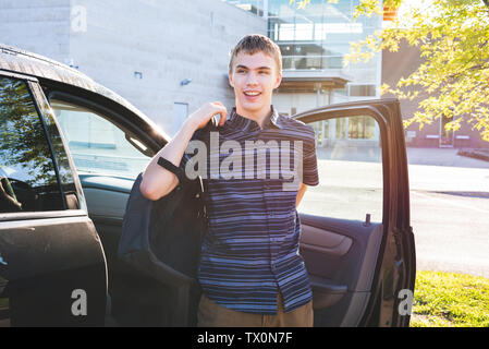 Felice adolescente di uscire la sua auto e la messa sul suo zaino come egli arriva a scuola la mattina. Foto Stock