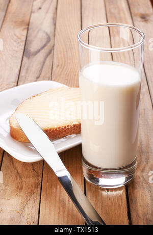 Toast con burro con un bicchiere di latte e di coltello sullo sfondo di legno Foto Stock