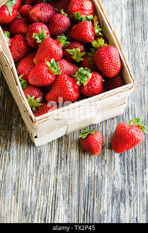 Fresche fragole mature in un cestello di legno su un sfondo di legno. Organici di bacche succosa. Vista dall'alto. Copia dello spazio per il tuo testo. Foto Stock