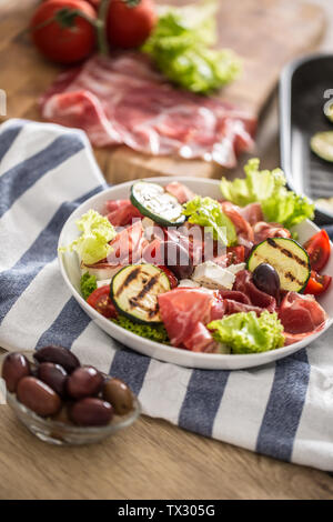 Fresca insalata di lattuga con zucchine grigliate coppa di Parma Prosciutto Formaggio feta olive pomodori e olio di oliva Foto Stock