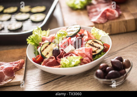 Fresca insalata di lattuga con zucchine grigliate coppa di Parma Prosciutto Formaggio feta olive pomodori e olio di oliva Foto Stock