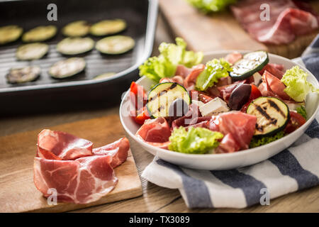 Fresca insalata di lattuga con zucchine grigliate coppa di Parma Prosciutto Formaggio feta olive pomodori e olio di oliva Foto Stock