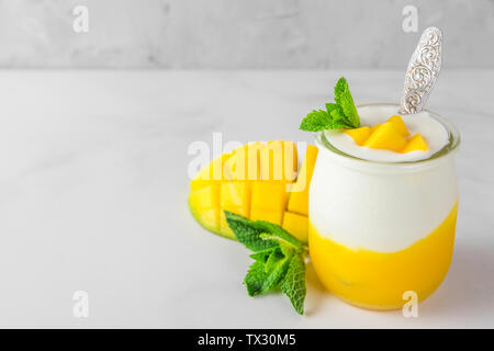 Frutta allo yogurt mango con menta fresca in un bicchiere con un cucchiaio sullo sfondo di calcestruzzo. Colazione sana. close up Foto Stock