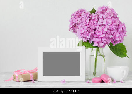 Moderna vita ancora di rosa fiori di ortensie, photo frame, tazza di caffè e confezione regalo bianca sul tavolo di legno con copia spazio. vacanza o nozze backgrou Foto Stock