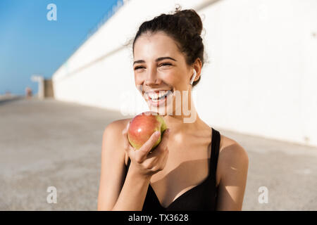 Attraente sorridente sportive riposo dopo l'allenamento all'aperto, che mostra apple Foto Stock