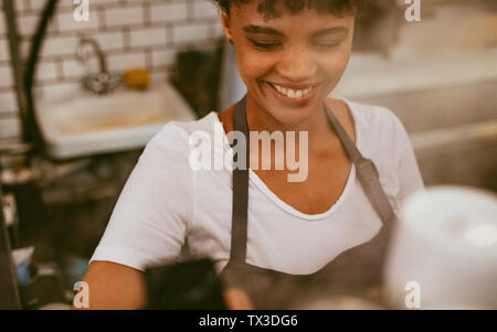 Felice giovane donna in grembiule lavorando presso la caffetteria. Barista femmina lavorando presso la caffetteria. Foto Stock