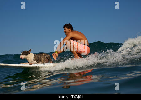 Giovane uomo e cane a cavallo con la tavola da surf sulle onde dell'oceano Foto Stock