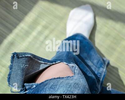 Donna vestita di un jeans blu con un grande foro al di sotto del ginocchio sulla sinistra una gamba pant. Holey jeans. Vista dall'alto in basso. Foto Stock