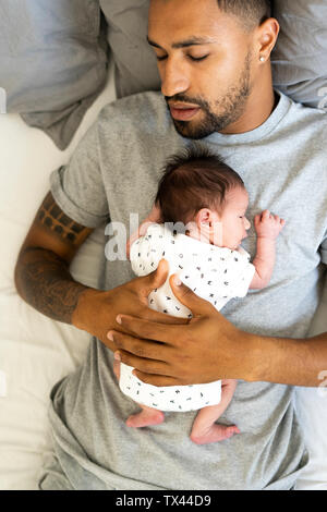 Uomo dorme nel letto tenendo il suo neonato Foto Stock