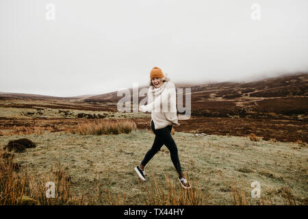 Regno Unito, Scozia, Isola di Skye, felice giovane donna in esecuzione nel paesaggio rurale Foto Stock