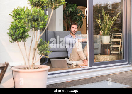 Giovane uomo rilassante nella sua casa confortevole, guardando fuori della finestra Foto Stock