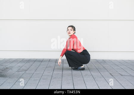 Elegante giovane donna accovacciata davanti a una parete Foto Stock