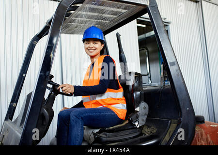 Ritratto di fiducia lavoratore di sesso femminile che sul carrello elevatore a forche in fabbrica Foto Stock