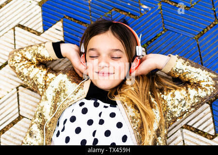 Ritratto di felice ragazza indossando golden sequin jacket ascoltando musica con le cuffie Foto Stock