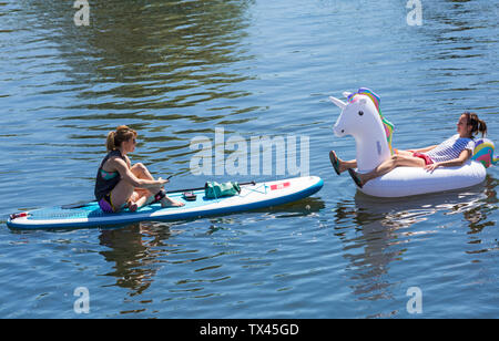 Donna paddleboarder paddle boarder e gonfiabili gonfiabile unicorn relax su Dorset Dinghy giorno al fiume Stour, Iford, Dorset Regno Unito nel mese di giugno Foto Stock