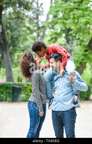 Padre figlio portante sovrapponibile in un parco, mentre il figlio sta baciando la sua madre Foto Stock