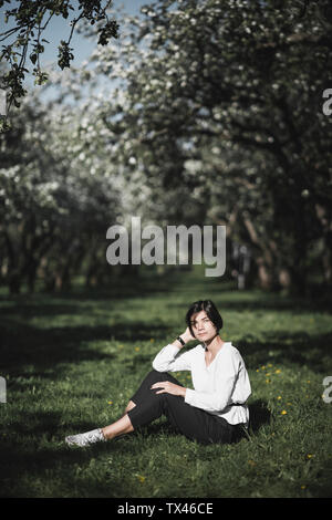 Donna seduta sul prato tra alberi di mele Foto Stock