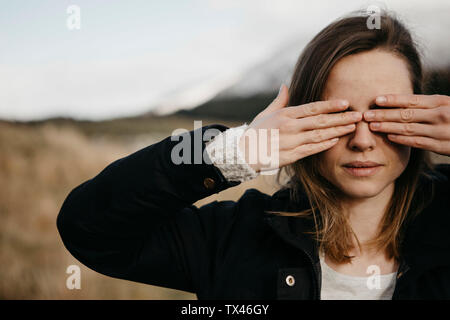 Regno Unito, Scozia, giovane donna che copre i suoi occhi nel paesaggio rurale Foto Stock