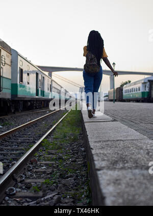 Vista posteriore della giovane donna a piedi a bordo della ferrovia presso la stazione ferroviaria Foto Stock