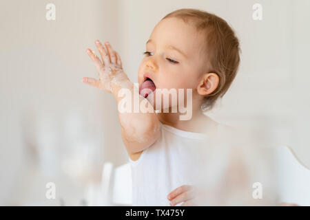 Bambina leccare il suo braccio mentre si effettua una torta in cucina a casa Foto Stock