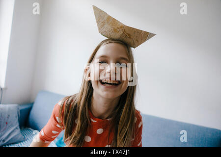 Felice ragazza di bilanciamento barca di carta sul suo capo a casa Foto Stock