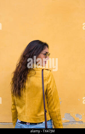 Ritratto di giovane donna che indossa il giallo giacca di pelle e occhiali da sole e vista posteriore Foto Stock