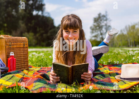 Giovane donna sdraiata su una coperta picnic, la lettura di un libro in un parco Foto Stock