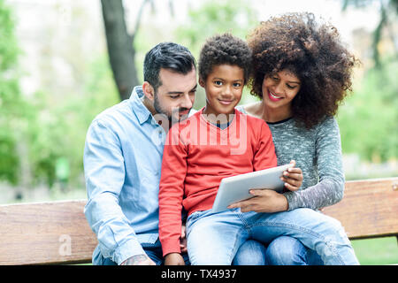 Famiglia seduta su una panchina nel parco, utilizzando tavoletta digitale Foto Stock