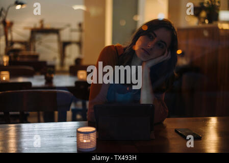 Grave giovane donna seduta a tavola in un ristorante utilizzando tablet Foto Stock