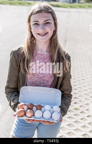 Ritratto di ragazza sorridente con bretella mostra box con uova Foto Stock