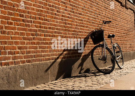 Danimarca, Copenaghen, bicicletta appoggiata contro un muro di mattoni a luce solare Foto Stock