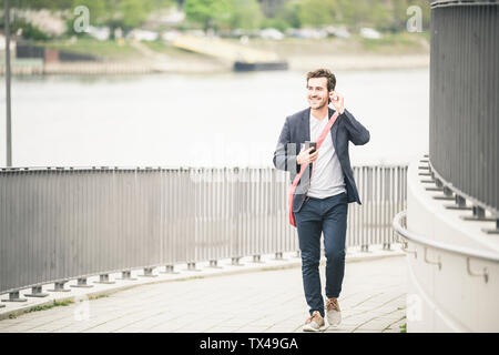 Imprenditore a camminare in città con un telefono cellulare e auricolari Foto Stock