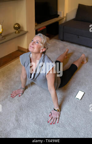 Donna matura facendo esercizi Yoga nella stanza vivente Foto Stock